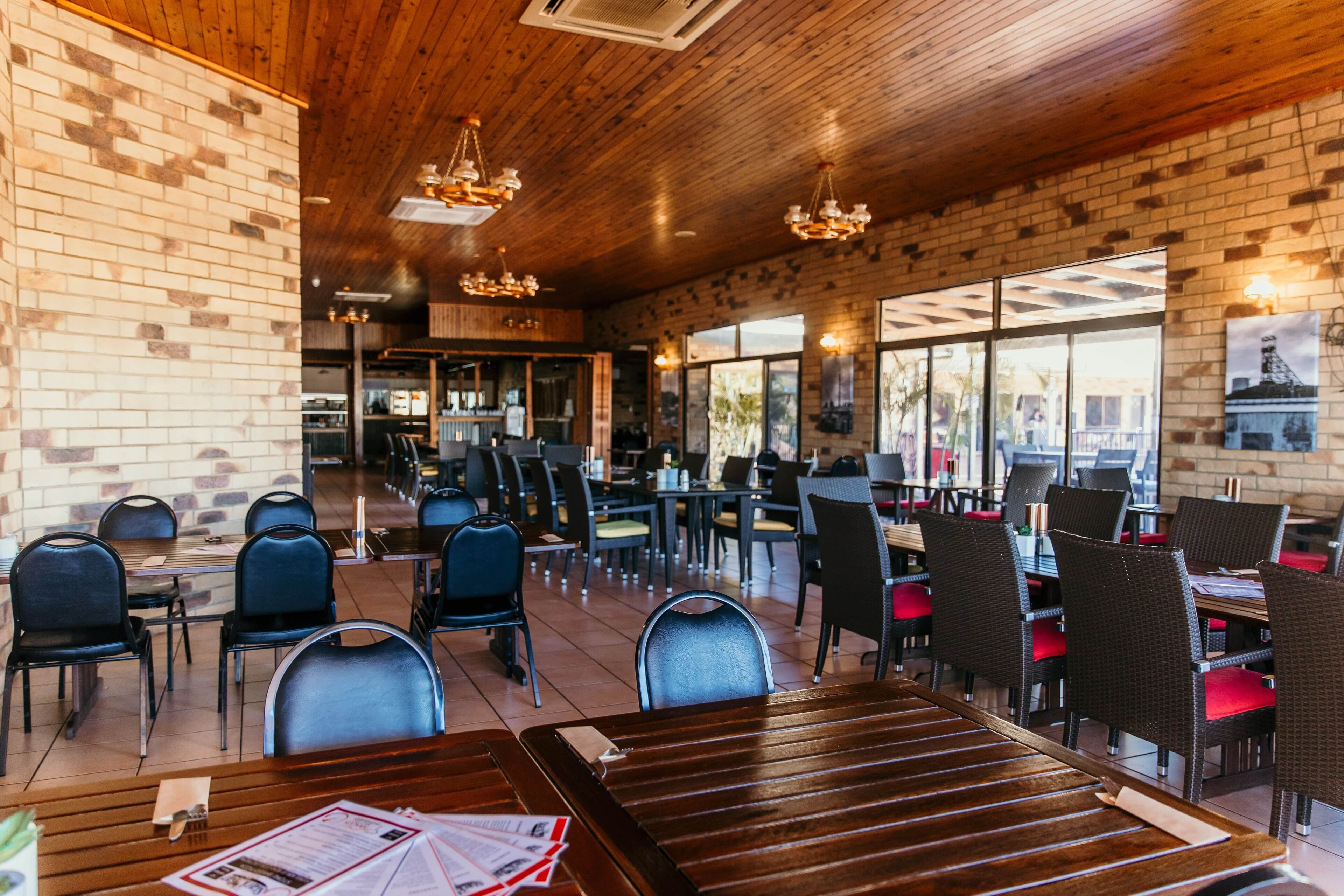 A restaurant with brick walls, wooden ceiling, and multiple tables and chairs.