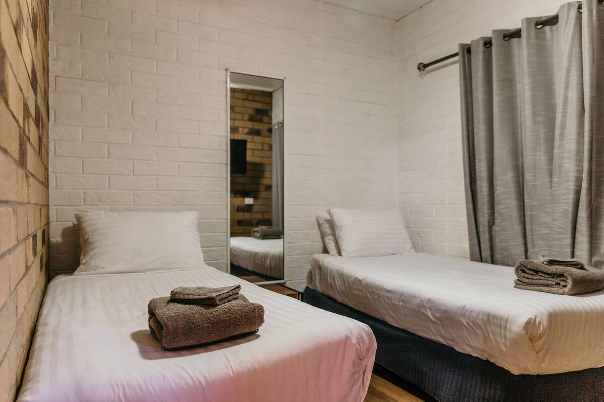 A hotel room with two beds, white bedding, a mirror, and a curtain.