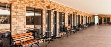 A long corridor with a brick wall, multiple doors, and rows of tables and chairs.