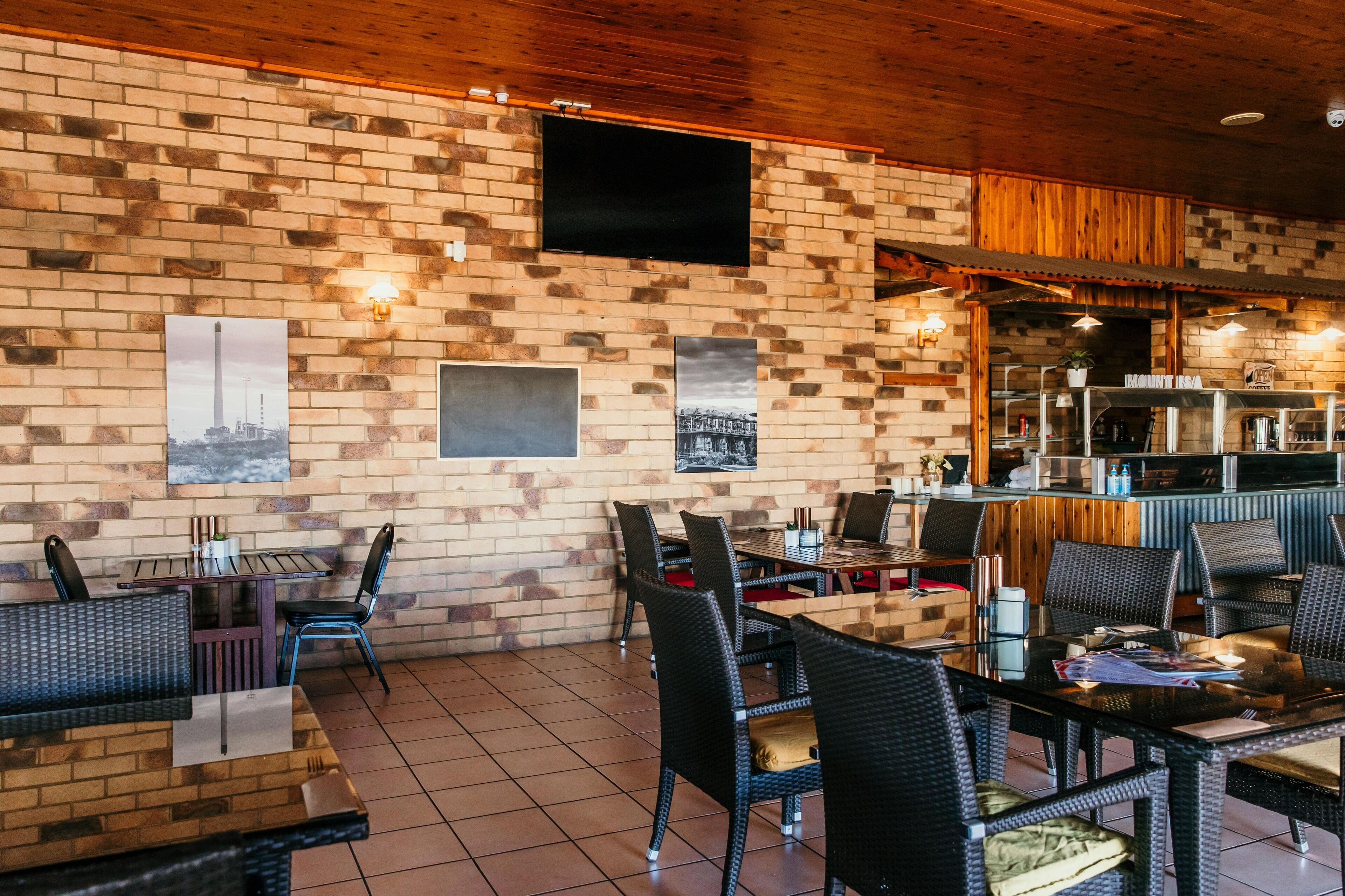 A restaurant with brick walls, black wicker furniture, and a flat-screen TV mounted on the wall.