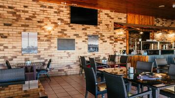 A restaurant with brick walls, black wicker furniture, and a flat-screen TV mounted on the wall.