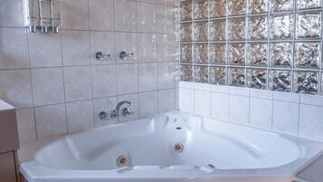Un baño con una bañera grande, ducha y pared de bloques de vidrio.