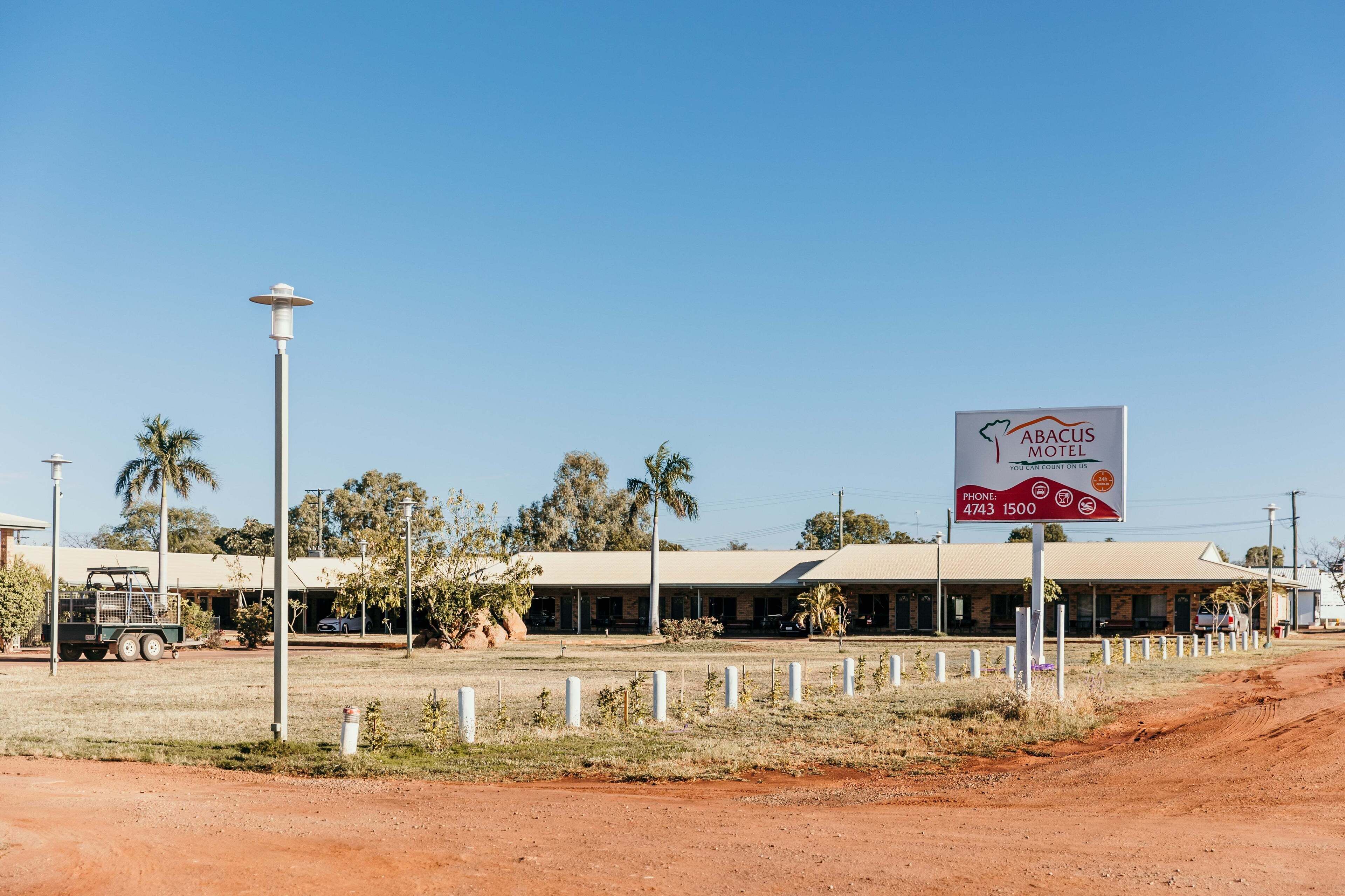 A motel with a signboard, a dirt road, and a few vehicles.