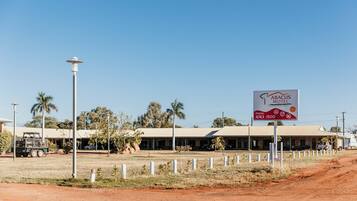 A motel with a signboard, a dirt road, and a few vehicles.