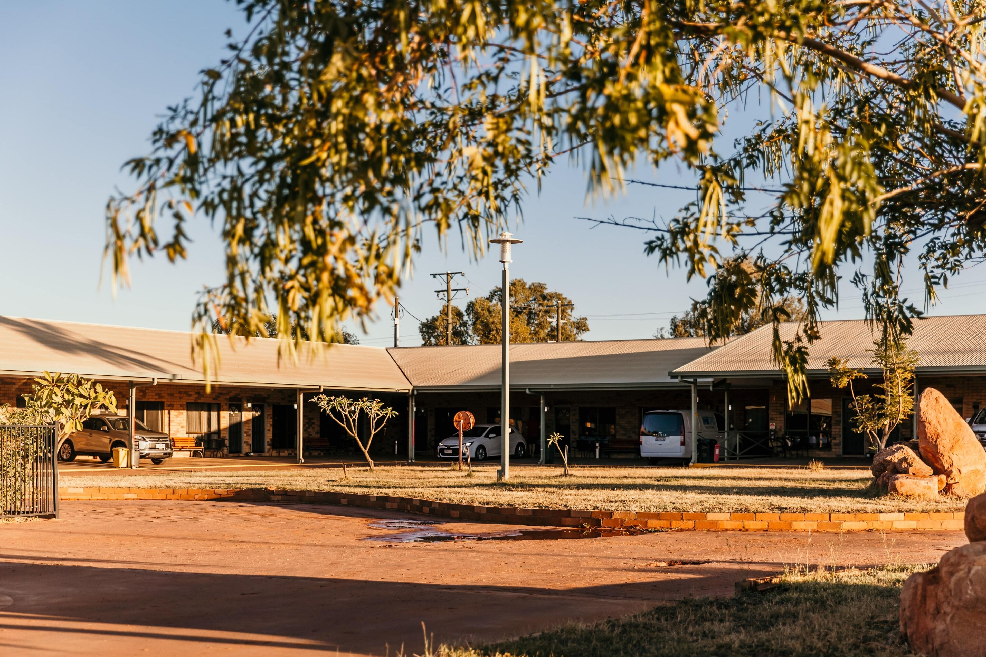 Um edifício com área de estacionamento coberta, um poste de luz e uma rocha grande em primeiro plano.