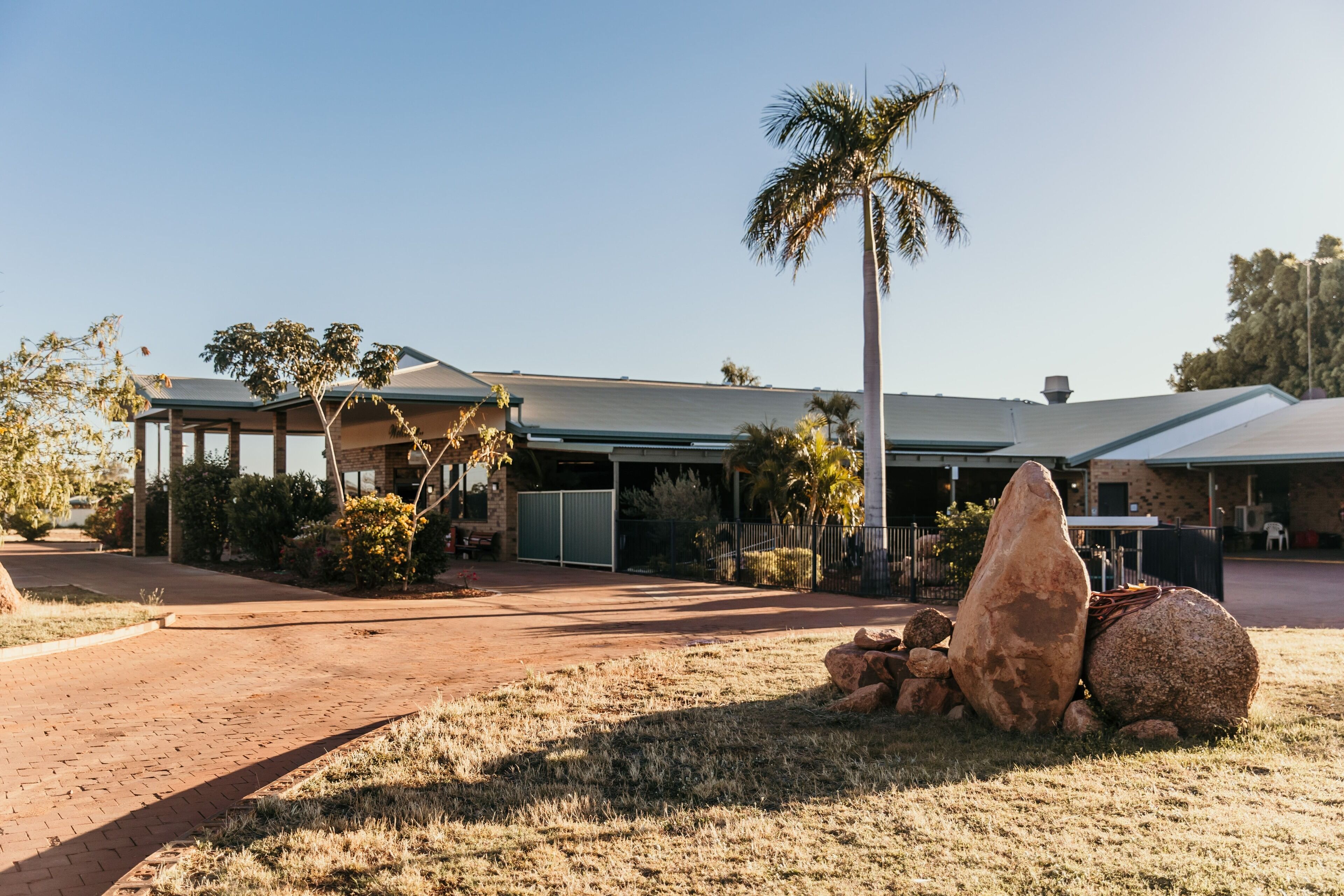 A building with a covered patio area, large rocks in the foreground, and a palm tree.