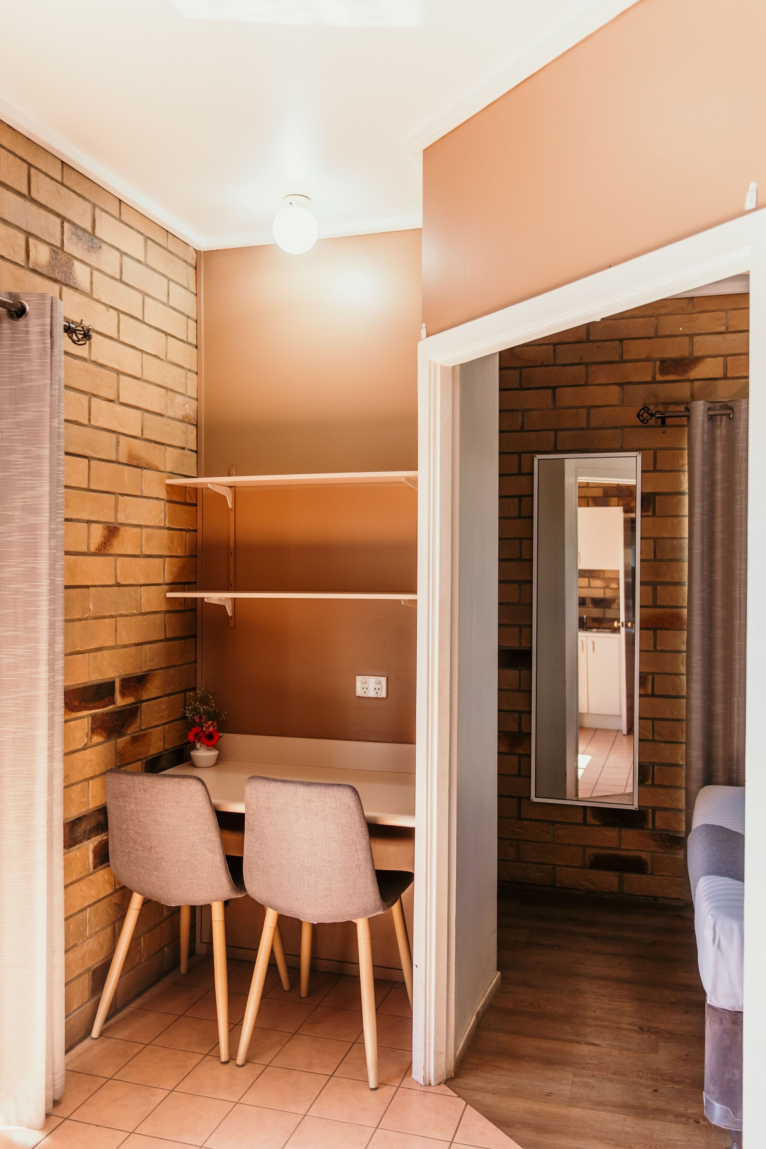 Una habitación con pared de ladrillo, suelo de madera, una mesa con sillas y un espejo en la pared.