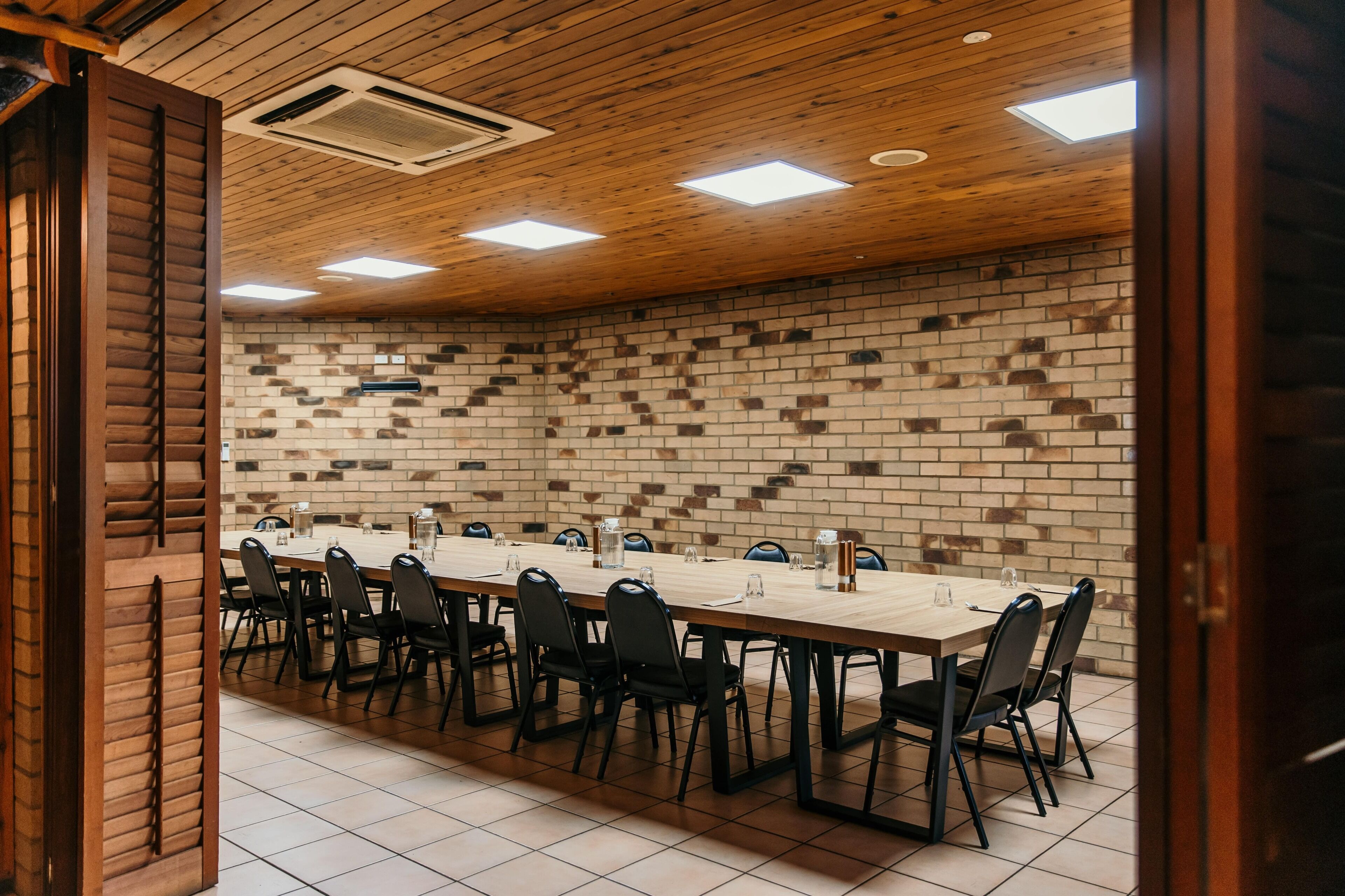 A conference room with a long table, black chairs, and a brick wall.