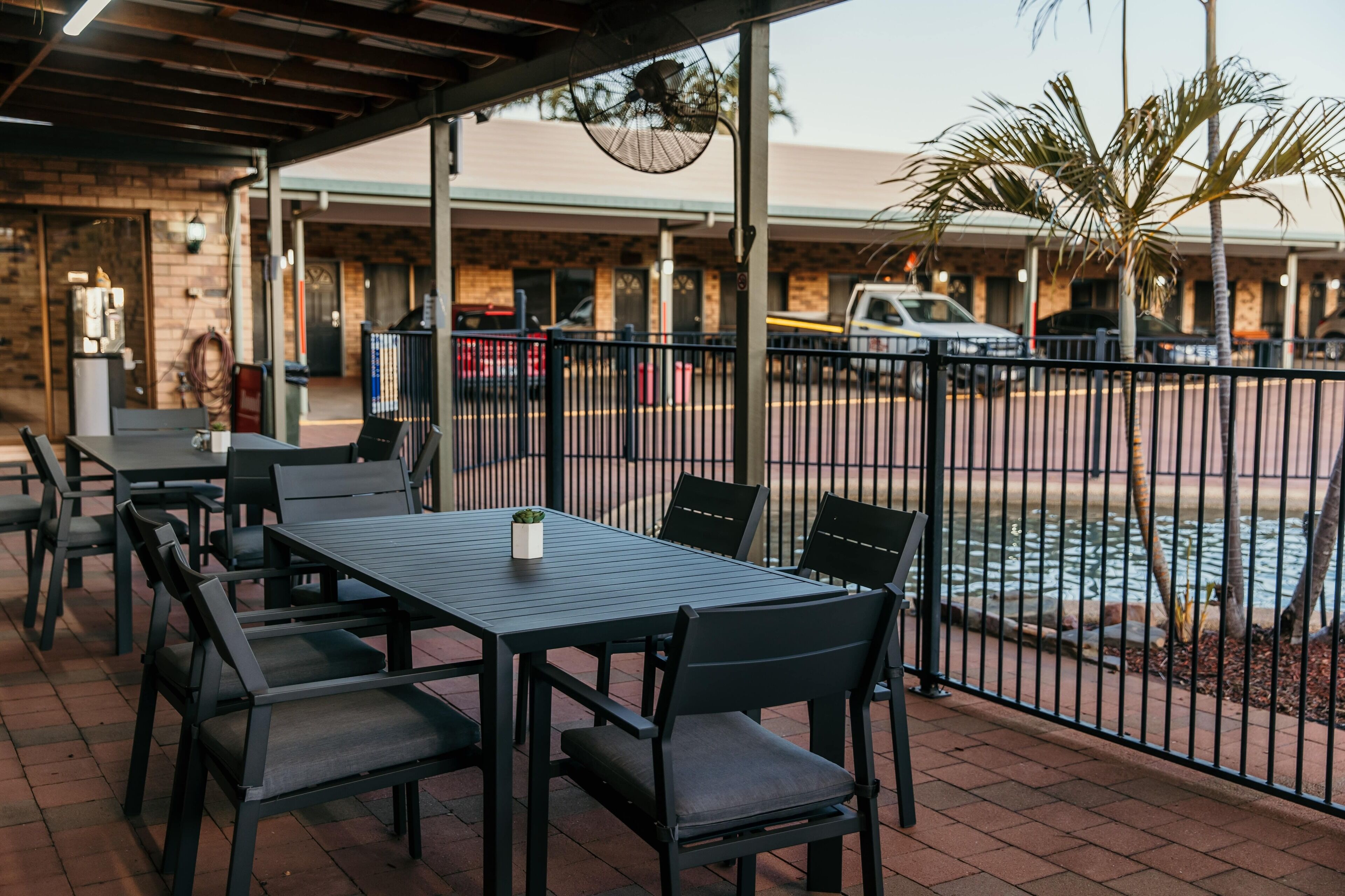 An outdoor patio area with a table and chairs, a covered seating area, and a view of a parking lot with vehicles.