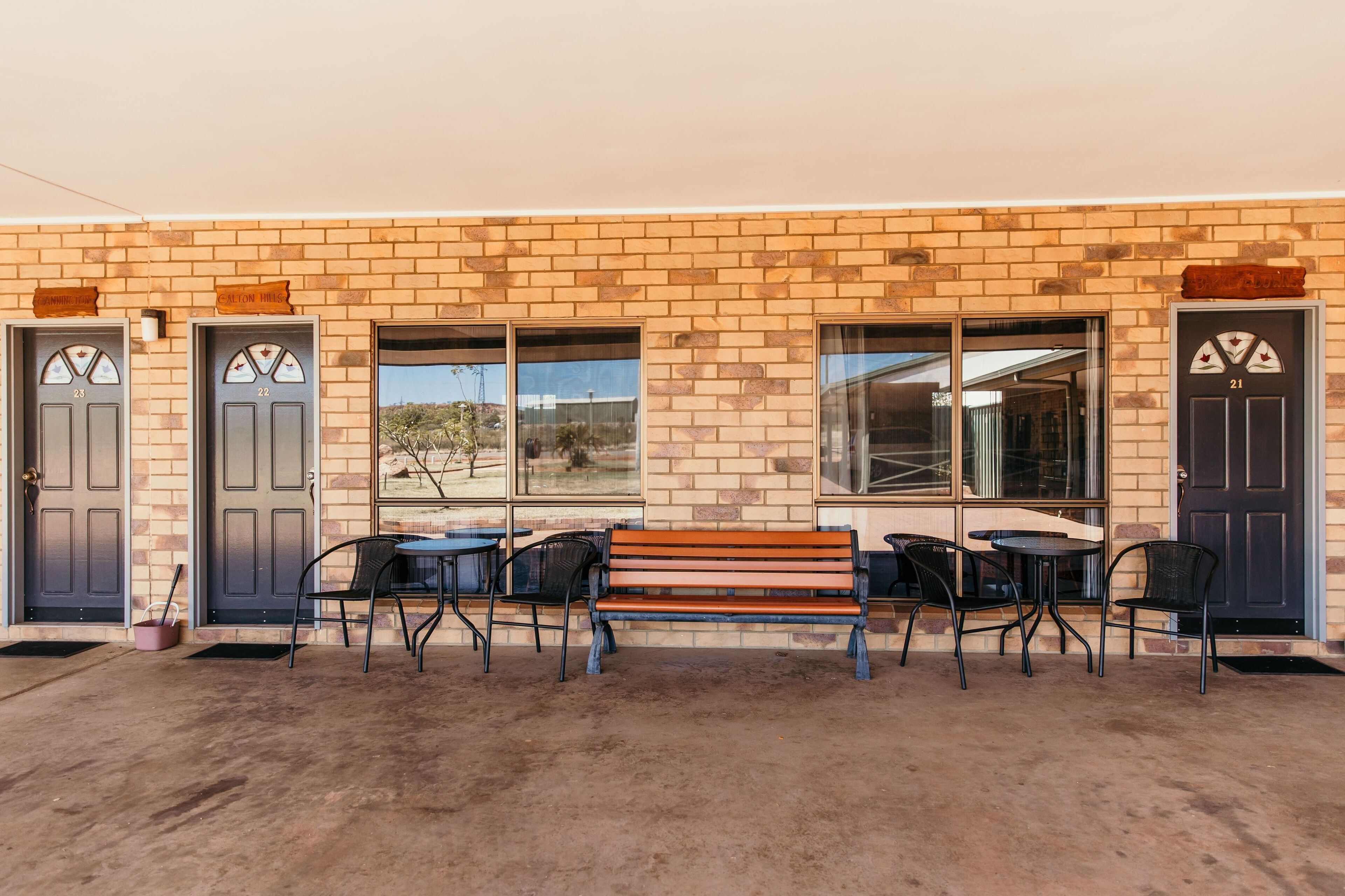 A building with a brick facade, numbered doors, and a bench with chairs outside.