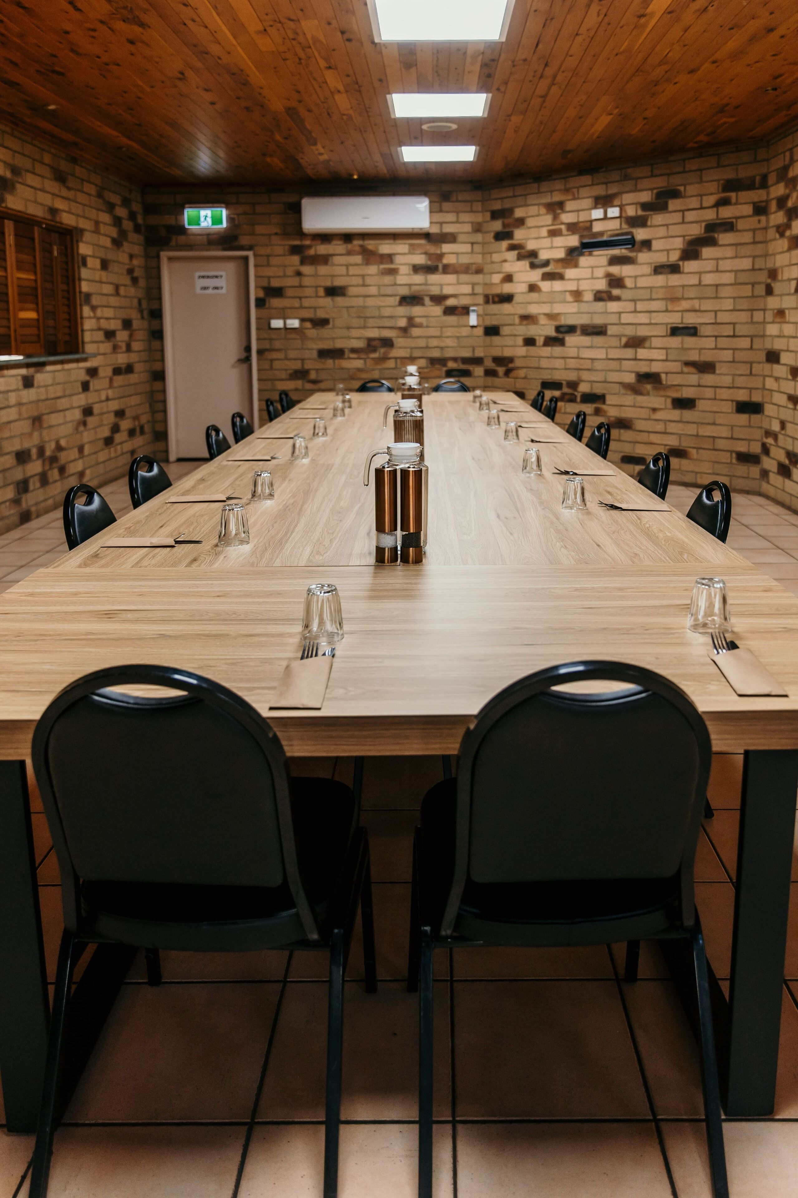 Ein Konferenzraum mit einem langen Holztisch, schwarzen Stühlen und einer Backsteinwand.
