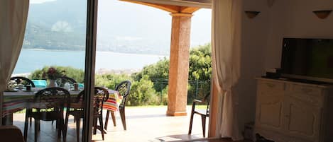 Una habitación con vistas a un lago y montañas, un comedor con mesa y sillas, y un televisor sobre un mueble.