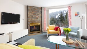 A modern living room with a fireplace, a flat-screen TV, a sofa, and a glass coffee table. - SUPER SUMMER GETAWAY  Views + POOL + HOT TUB (WD, FP) (Whistler)