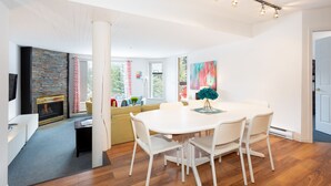 A modern living room with a fireplace, a dining area with a white table and chairs, and a large window providing natural light. - SUPER SUMMER GETAWAY  Views + POOL + HOT TUB (WD, FP) (Whistler)