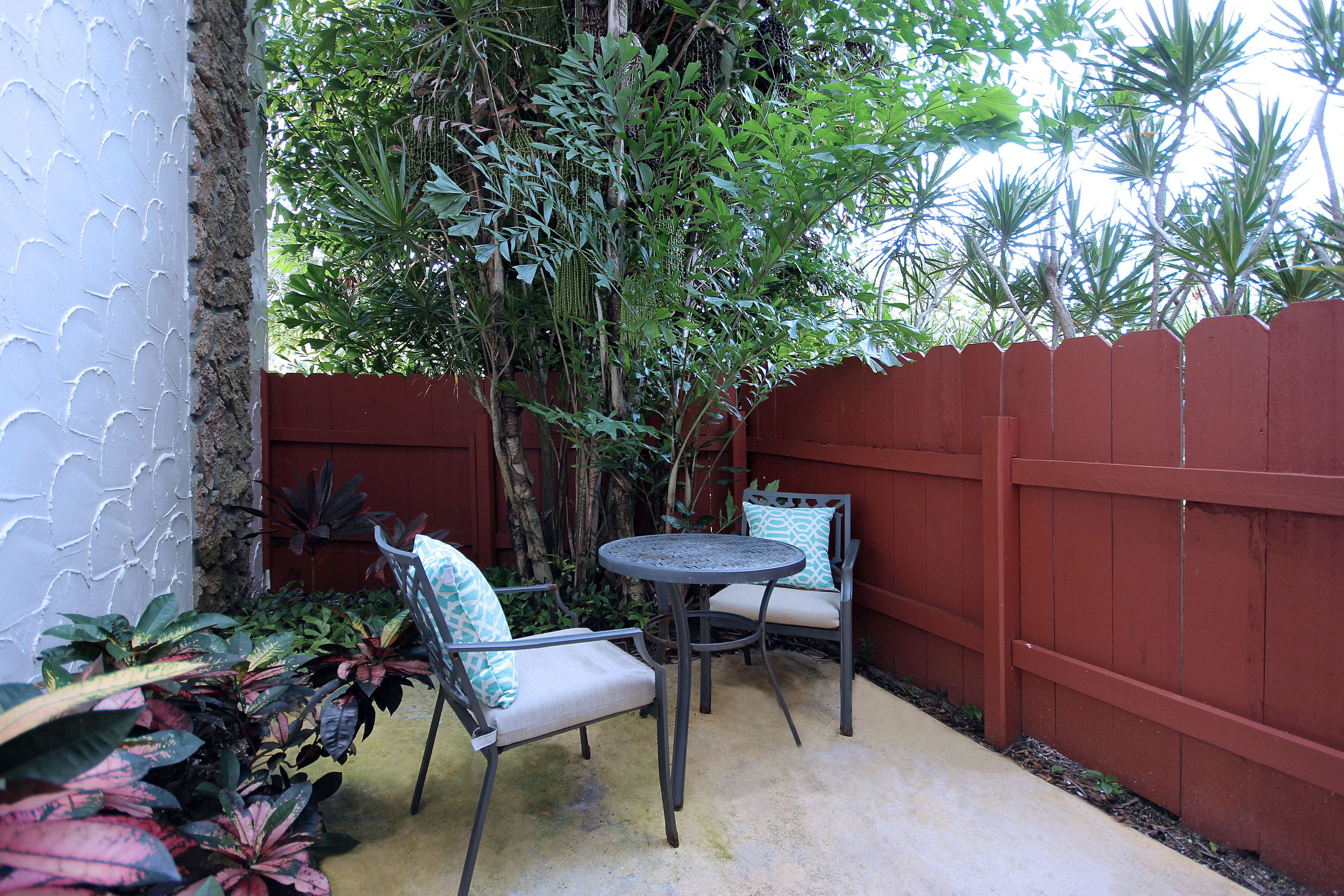 A patio with two chairs and a table, surrounded by a red fence and various plants.