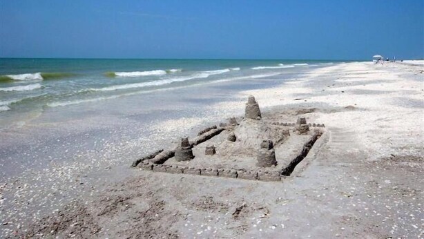 Una playa arenosa con una estructura peque ña y de aspecto antiguo al frente.