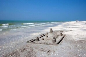 Una playa arenosa con una estructura pequeña y de aspecto antiguo al frente.