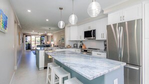 Una cocina moderna con una isla grande, electrodomésticos de acero inoxidable e iluminación colgante.