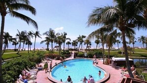 Zona de piscina con sillas de descanso y palmeras, rodeada por un jardín ajardinado y vistas al océano.