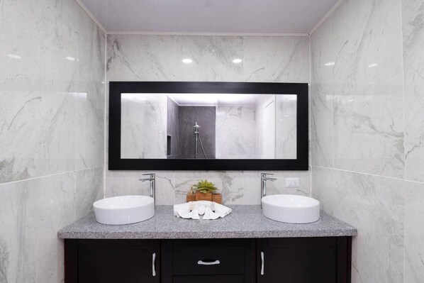 A bathroom with two sinks, a large mirror, and marble walls. - 1BR Beachfront Ocean View Apartment in Cabarete (Cabarete)
