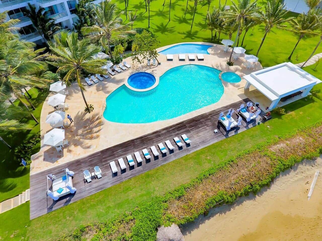 A swimming pool with lounge chairs and umbrellas, surrounded by palm trees and a pathway.