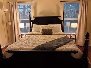 Een hemelbed met quilt, twee bedlampen en een raam met zonwering.
