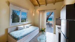A bedroom with a bed, a glass table with flowers, a view of the beach, and a kitchen area. - Makis&Fani Homes (Lefkada)