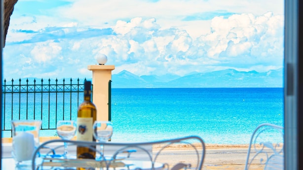 A seaside view with a table set for dining, a bottle of wine, and glasses. - Makis&Fani Homes (Lefkada)