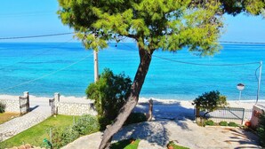 A coastal property with a stone pathway leading to a beach, a tree in the foreground, and a clear view of the sea. - Makis&Fani Homes (Lefkada)