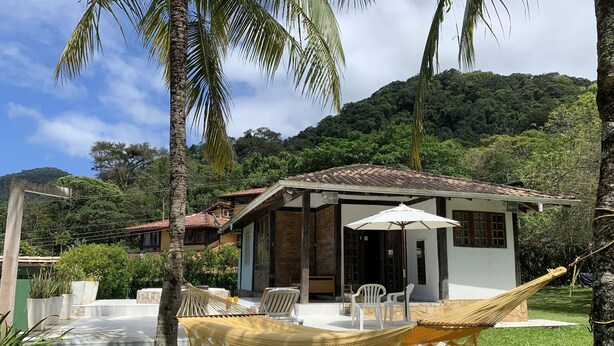 A small house with a porch, a hammock, and a view of a forested hill. - HOUSE WITH JACUZZI - SOLARIUM AND PRIVATIVE TENNIS COURT (Praia de Maresias)