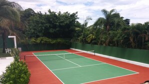 A tennis court with a green and red surface, surrounded by dense tropical foliage. - HOUSE WITH JACUZZI - SOLARIUM AND PRIVATIVE TENNIS COURT (Praia de Maresias)