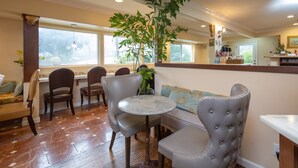 A dining area with a round table and chairs, a sofa, and a large plant. - Vendange Carmel Inn & Suites (Carmel)