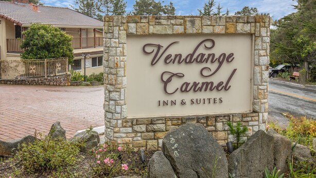 A sign for Vendange Carmel Inn & Suites, surrounded by a stone wall and landscaping. - Vendange Carmel Inn & Suites (Carmel)