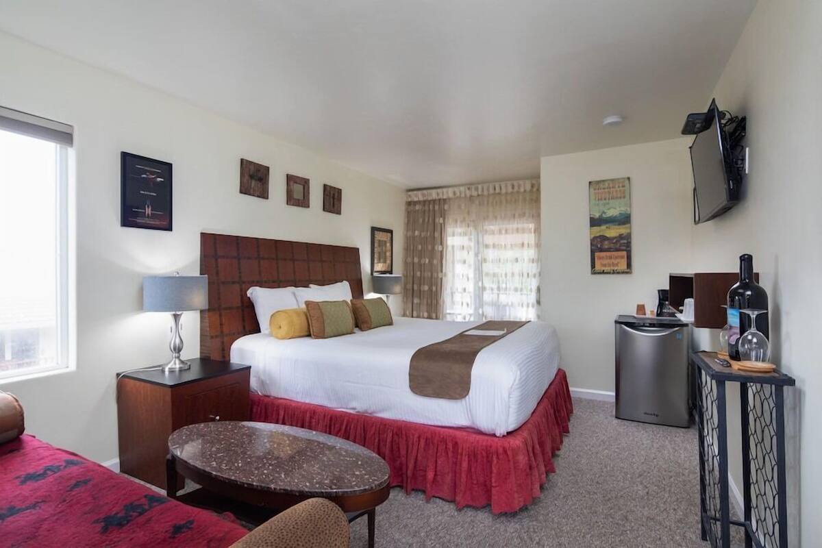 A hotel room with a bed, bedside table, lamp, TV, and a small table.