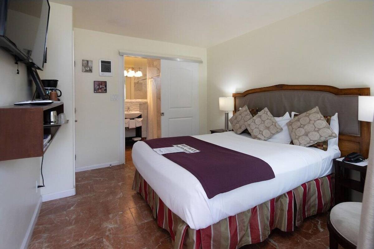 A hotel room with a bed, bedside table, lamp, and a view of the bathroom.