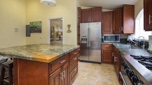 A kitchen with wooden cabinets, a stainless steel refrigerator, a microwave, and a granite countertop. - Vendange Carmel Inn & Suites (Carmel)