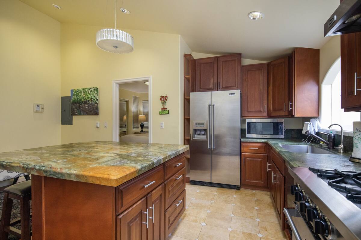 A kitchen with wooden cabinets, a stainless steel refrigerator, a microwave, and a granite countertop.