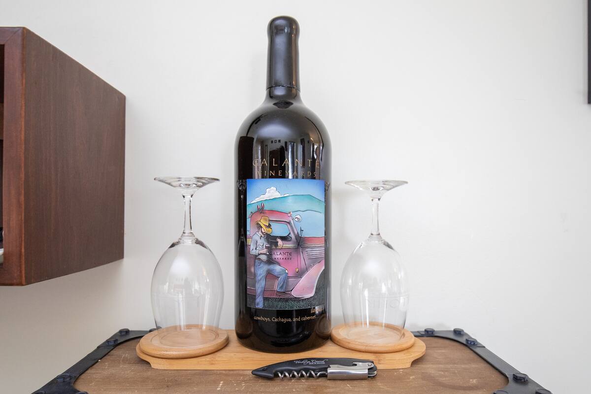 A wine bottle with a cowboy illustration on the label, two wine glasses, and a knife on a wooden surface.