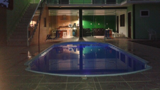 A swimming pool with a glass barrier, a staircase leading to a balcony, and a view of the interior of a building with a green wall and a kitchen area. - House in Balneário Barra do Sul - SC  (Balneário Barra do Sul)