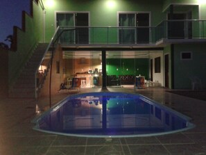 Une piscine séparée par une paroi en verre, un escalier menant à un balcon et une vue sur l’intérieur d’un bâtiment doté d’un mur végétal et d’un espace cuisine.