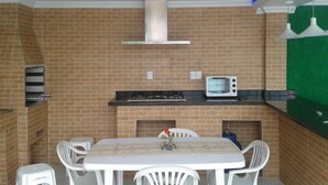 A kitchen with a brick wall, a gas stove, a microwave, and a white table with chairs. - House in Balneário Barra do Sul - SC  (Balneário Barra do Sul)