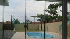 A swimming pool with a tiled patio area, a fenced yard, and a building with a glass door. - House in Balneário Barra do Sul - SC  (Balneário Barra do Sul)