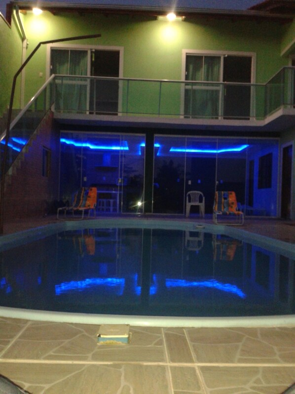 Une piscine intérieure avec une paroi en verre, un escalier menant à un balcon et un espace aménagé au bord de la piscine avec des chaises longues.