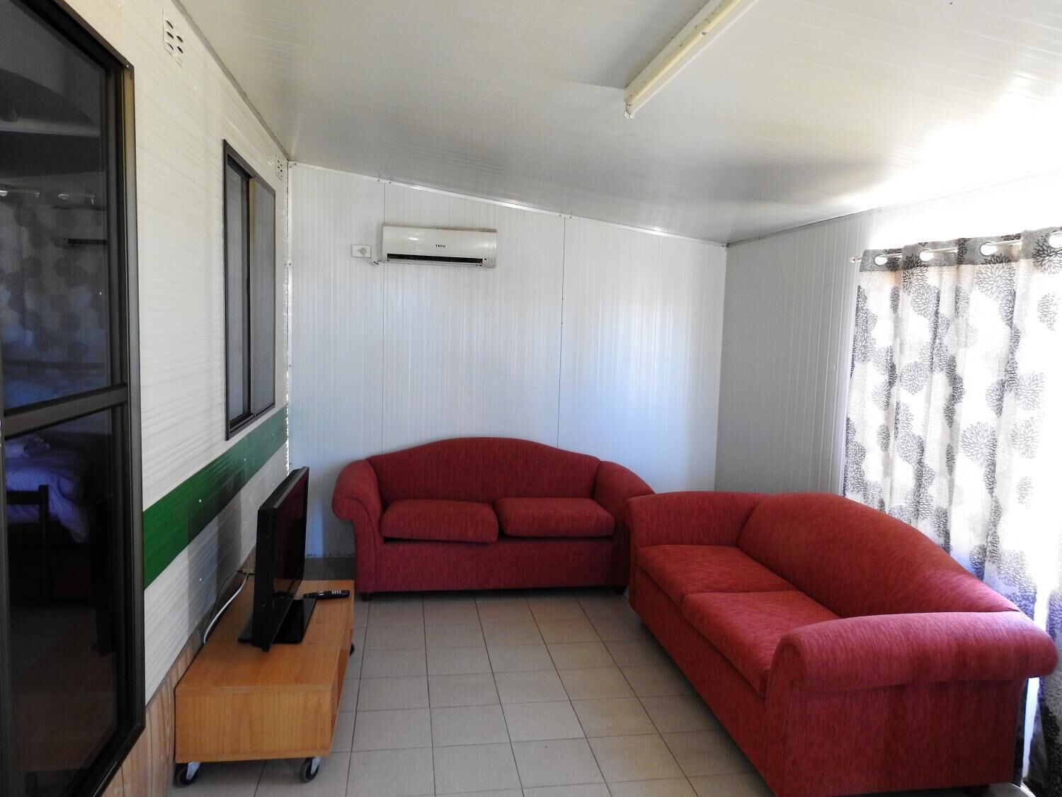 A compact living space with a red sofa, a small wooden table with a television, and an air conditioning unit on the wall.