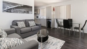 Ett modernt vardagsrum med en grå soffa, ett soffbord i glas och en tavla med en stadsbild på väggen.