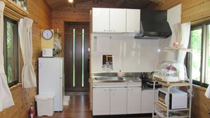 A compact kitchen with white cabinets, a stainless steel sink, and a microwave on a cart.