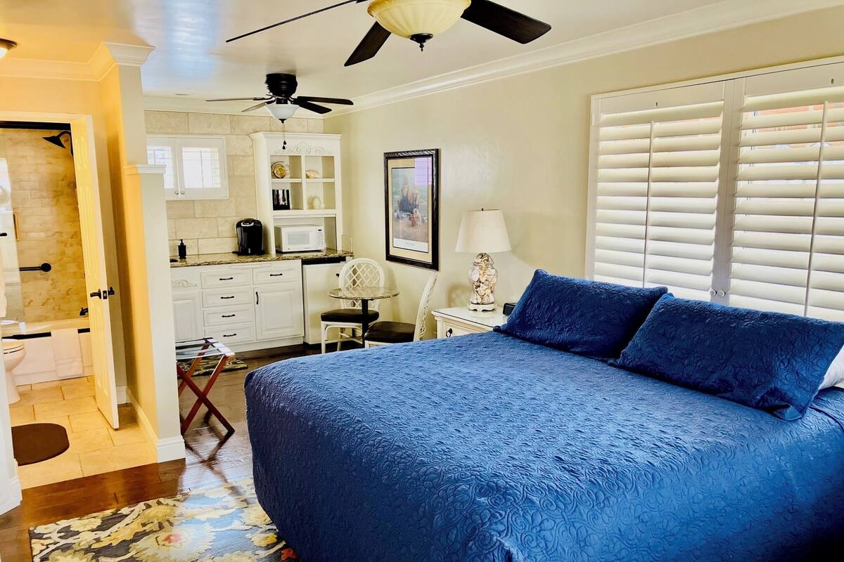 A bedroom with a large bed, a desk, a chair, and a ceiling fan.