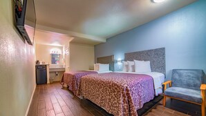 Een hotelkamer met twee bedden, een stoel, een bureau en een kleine kitchenette.