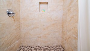 Douchegedeelte met beige tegels en een klein plankje met toiletartikelen.