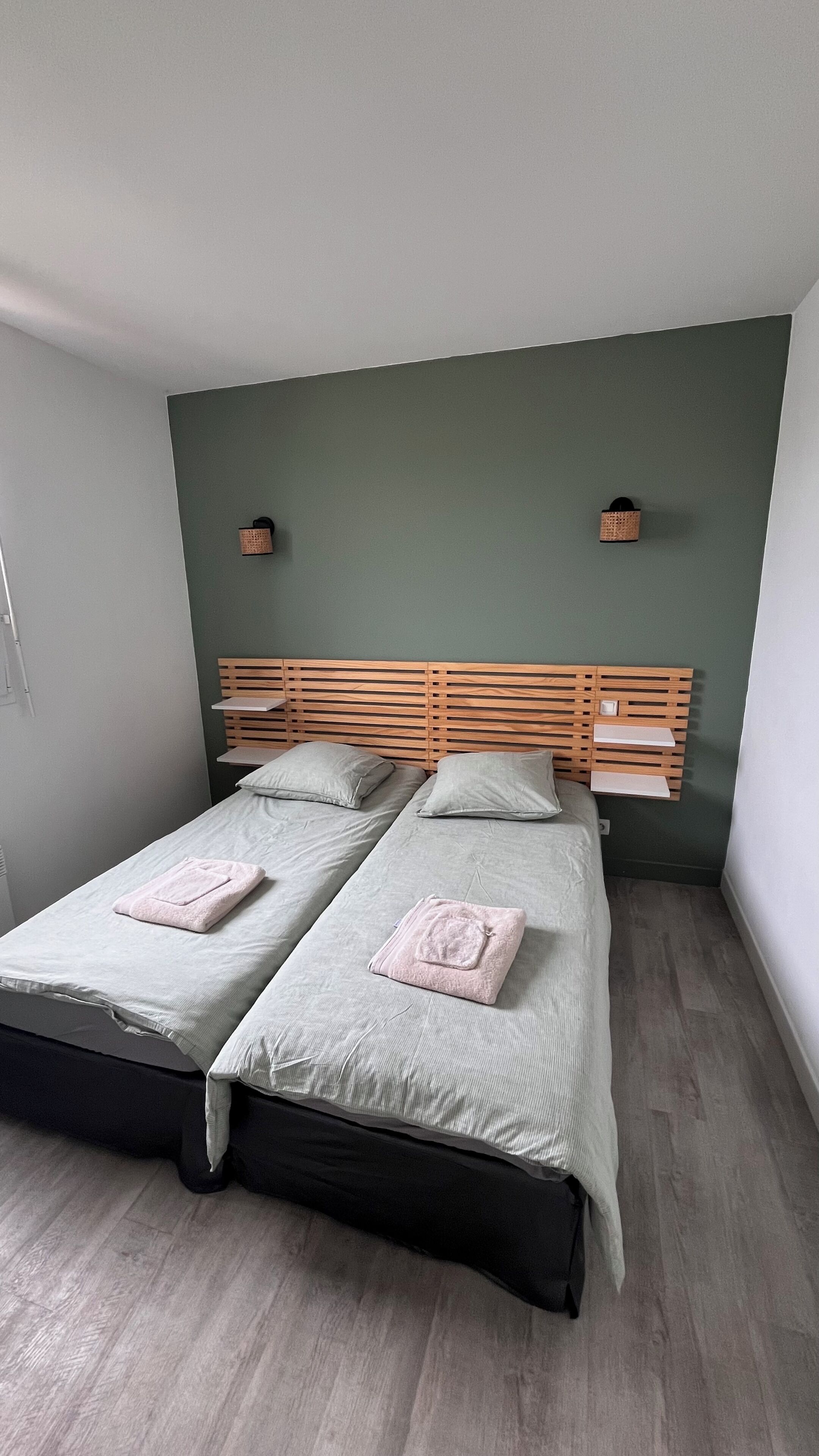 A double bed with a wooden headboard, two bedside tables, and a green wall.